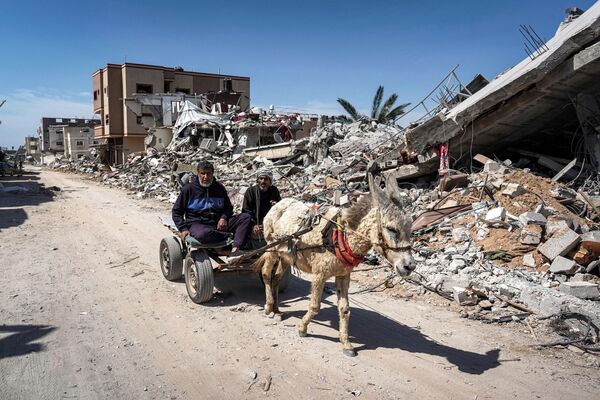 Two men sit in a donkey-drawn cart moving past the rubble of a demolished building. - Sputnik International