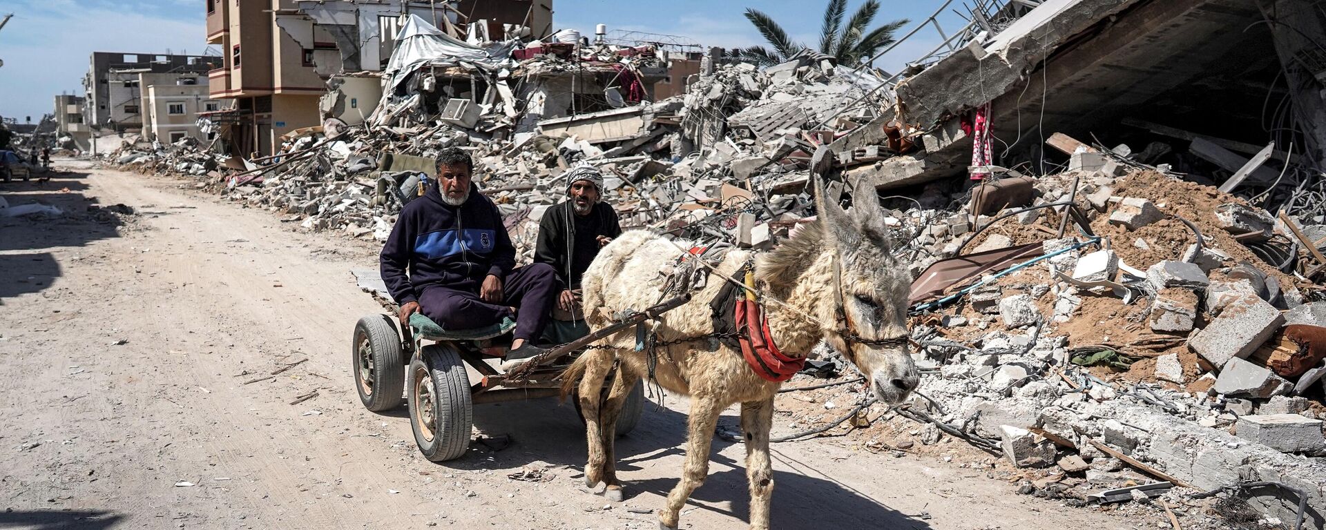 Two men sit in a donkey-drawn cart moving past the rubble of a destroyed building in Khan Yunis - Sputnik International, 1920, 26.04.2024