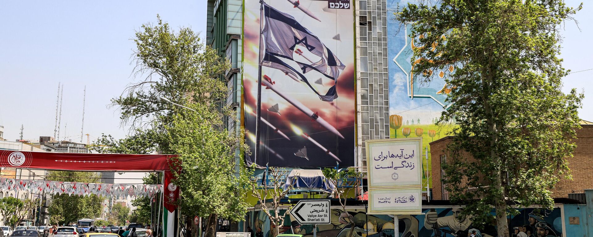 Vehicles drive past a building showing a banner depicting missiles and drones flying past a torn Israeli flag, with text in Persian reading the next slap will be harder and in Hebrew your next mistake will be the end of your fake state, in Palestine Square in Tehran on April 14, 2024. - Sputnik International, 1920, 14.04.2024