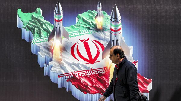 A man walks past a banner depicting missiles launching from a representation of the map of Iran coloured with the Iranian flag in central Tehran on April 15, 2024 - Sputnik International