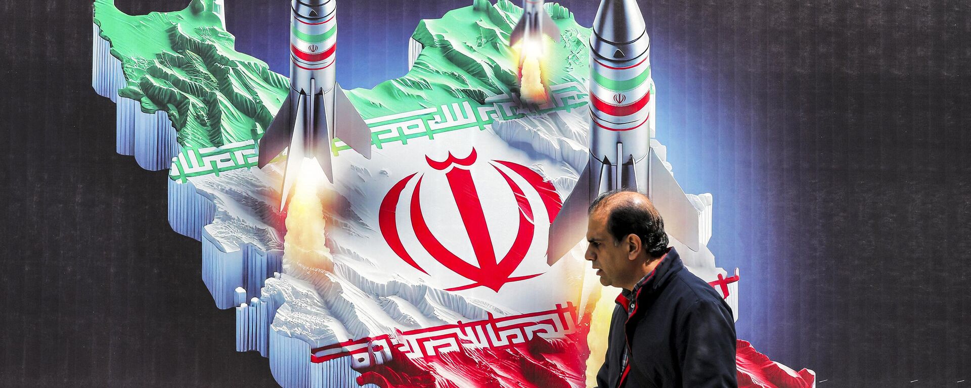 مردی از کنار بنری می گذرد که نشان دهنده پرتاب موشک از تصویر نقشه ایران با رنگ های پرچم ایران در مرکز شهر تهران در 15 آوریل 2024 - Sputnik International 1920 2024/04/19