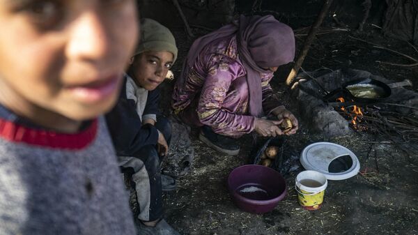 A displaced Syrian woman uses wood twigs for cooking as children look on, at the Al-Younani camp on the outskirts of the northern city of Raqa, amid a shortage of fuel and gas, on February 8, 2024. - Sputnik International