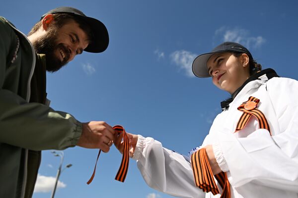 A Moscow campaign volunteer offers a St. George Ribbon to a local resident. - Sputnik International