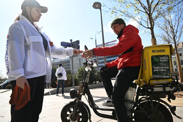 A volunteer handing out a St. George Ribbon to a delivery driver in Moscow.  - Sputnik International