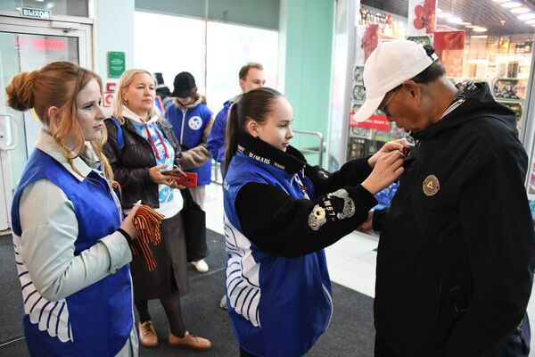 Activists of Russia&#x27;s national Victory Volunteers movement help a passerby with a St. George Ribbon in a Vladivostok mall. - Sputnik International