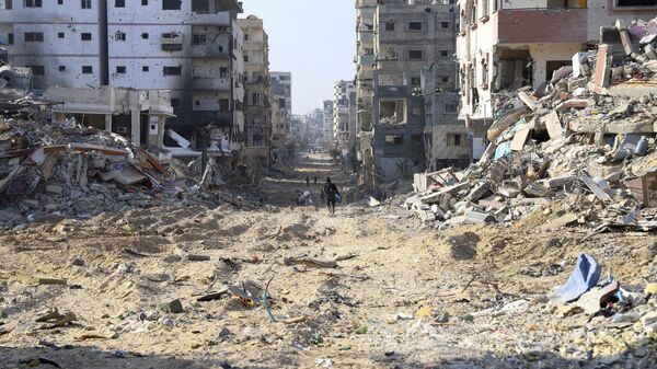 Palestinians walk between the remains of destroyed buildings following the Israeli bombardment on the main road of Gaza City on Tuesday, Jan. 2, 2024 - Sputnik International