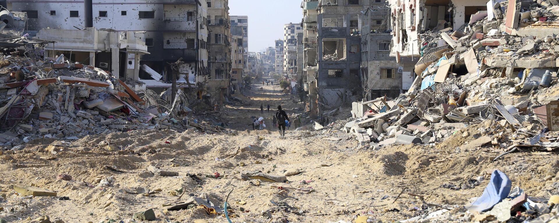 فلسطینیان در روز سه شنبه، 2 ژانویه 2024، بین بقایای ساختمان های ویران شده پس از بمباران اسرائیل در جاده اصلی شهر غزه قدم می زنند - Sputnik International 1920 2024/04/25