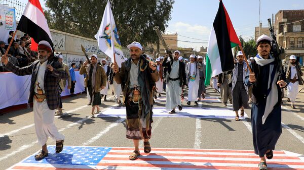 Armed Yemeni men step over a US and an Israeli flag painted on the asphalt in the Houthi-run capital Sanaa, during a march in support of the Palestinians amid ongoing battles between Israel and Hamas militants in the Gaza Strip, on February 29, 2024.  - Sputnik International