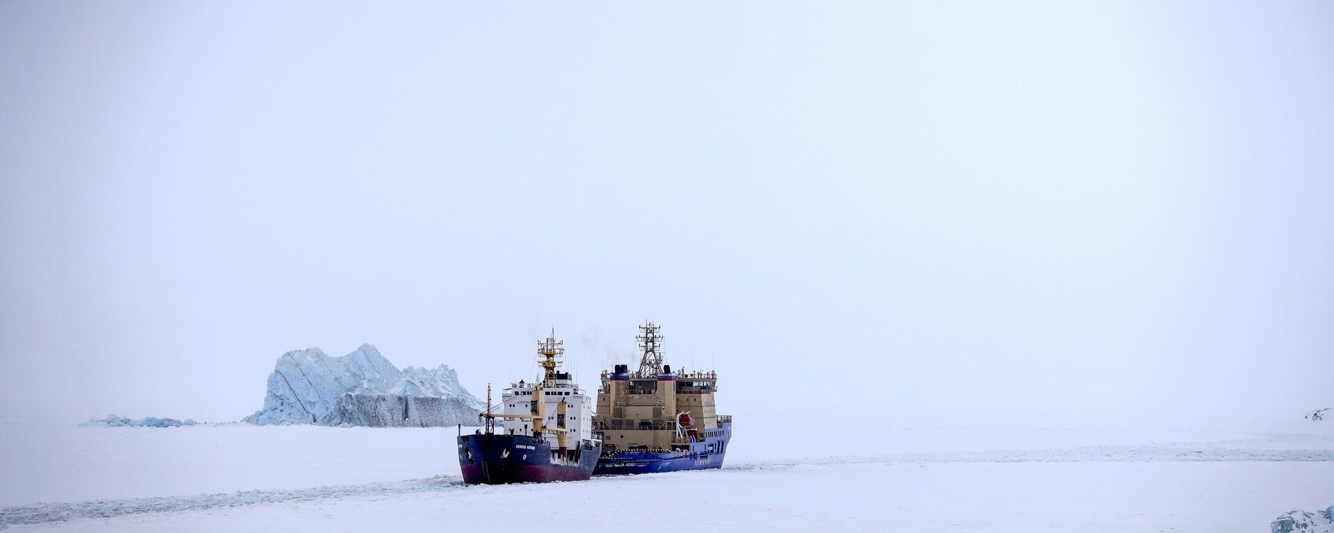 An Icebreaker making the path for a cargo ship with an iceberg in the background near a port on the Alexandra Land island near Nagurskoye, Russia, Monday, May 17, 2021. - Sputnik International, 1920, 17.05.2024