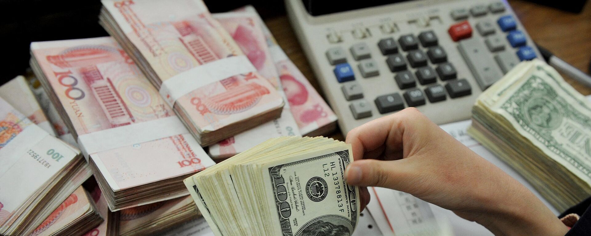 This photo taken n January 16, 2011 shows a bank teller counting stacks of US dollars and Chinese 100-yuan notes at a bank in Hefei, east China's Anhui province. - Sputnik International, 1920, 18.05.2024