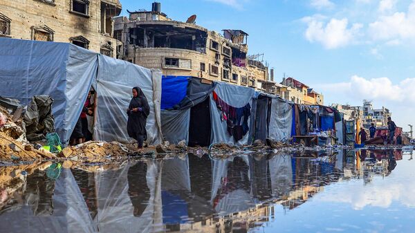 Palestinians circle a puddle in front of destroyed buildings and tents in Khan Younis, Palestine - Sputnik International