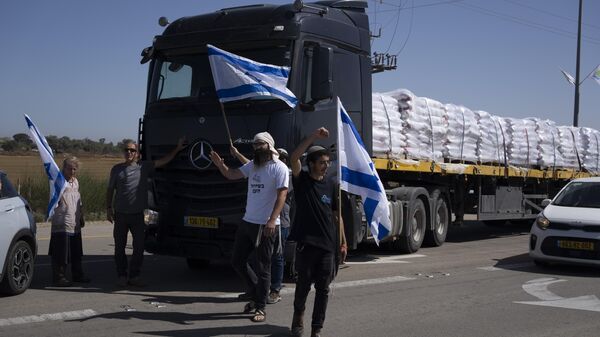 Holding Israeli flags people stand in front of trucks carrying humanitarian aid as they try to stop them from entering the Gaza Strip in an area near the Kerem Shalom border crossing in southern Israel, Thursday, May 9, 2024. (AP Photo/Leo Correa) - Sputnik International