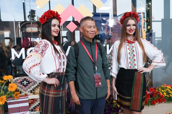 An international guest taking a photo with forum hosts dressed in traditional Russian regional female costumes. - Sputnik International