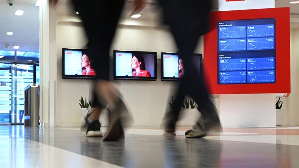 People walk past a screen showing currency exchange rates, share price index and other information is pictured in the office of the Moscow Exchange in Moscow, Russia. - Sputnik International