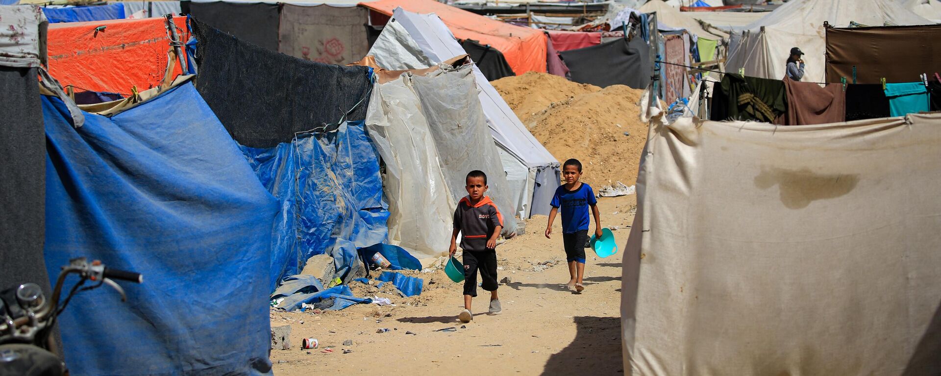 Palestinian children carry bowls as they walk past tents housing people who lost their homes, in the city of Khan Yunis, in the southern Gaza Strip on June 30, 2024, amid the ongoing conflict between Israel and the Palestinian Hamas militant group - Sputnik International, 1920, 29.07.2024