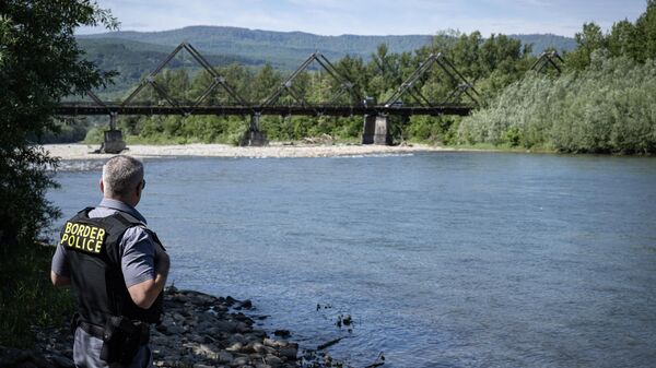 A Romanian border police officer inspects Tisa river's bank backdropped by the wooden bridge connecting Romania and Ukraine nearby the Sighetu Marmatiei border point on May 17, 2024 - Sputnik International