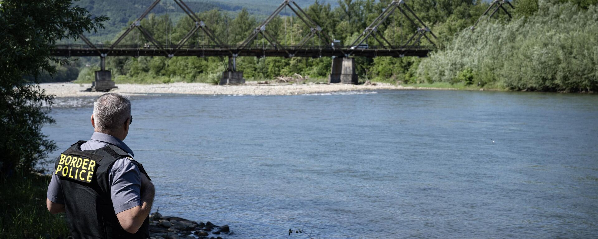 A Romanian border police officer inspects Tisa river's bank backdropped by the wooden bridge connecting Romania and Ukraine nearby the Sighetu Marmatiei border point on May 17, 2024 - Sputnik International, 1920, 14.07.2024