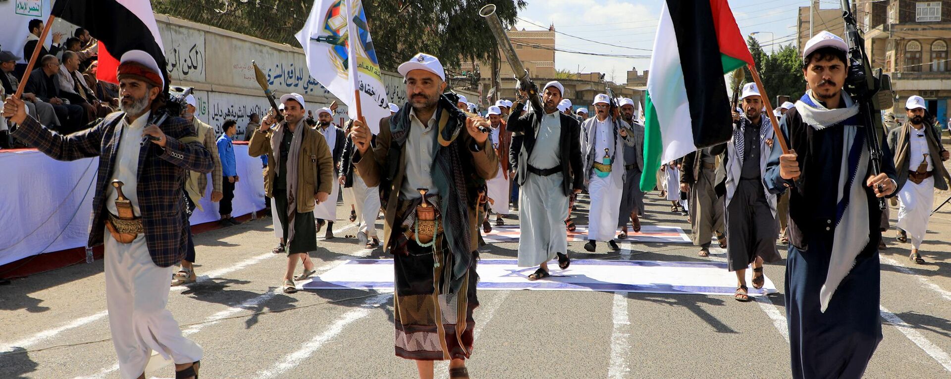 Armed Yemeni men step over a US and an Israeli flag painted on the asphalt in the Houthi-run capital Sanaa, during a march in support of the Palestinians amid ongoing battles between Israel and Hamas militants in the Gaza Strip, on February 29, 2024.  - Sputnik International, 1920, 28.07.2024