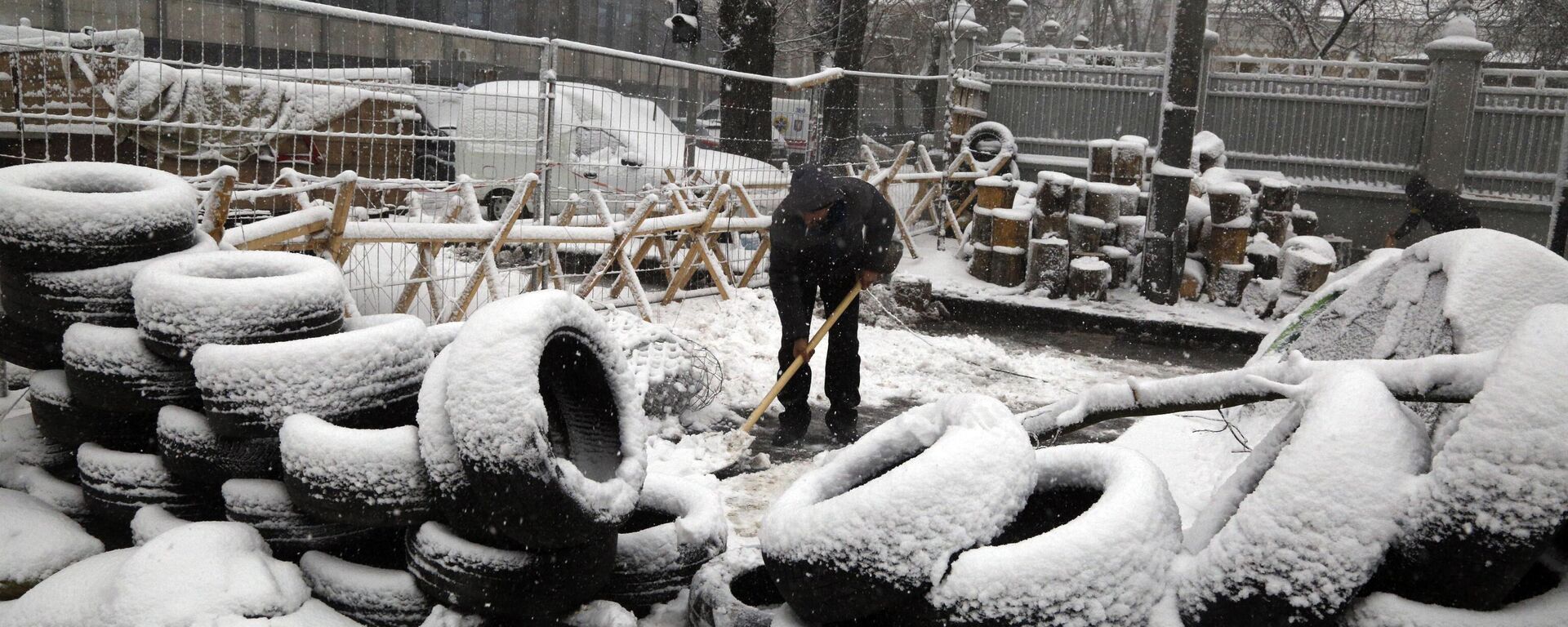 Under heavy snowfall an activist cleans away snow near a tire barricade erected by supporters of the Movement of New Forces, the political party led by Mikheil Saakashvili in front of the parliament building in Kiev, Ukraine, Monday, Dec.18, 2017 - Sputnik International, 1920, 26.08.2024