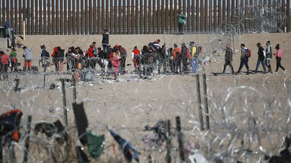 Migrants line up at the U.S. border wall after being detained by U.S. immigration authorities, seen from Ciudad Juarez, Mexico, Wednesday, Dec. 27, 2023. - Sputnik International