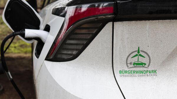 An electric car a logo of the Citizens' wind farm company stands at a charging station in Sprakebuell, Germany, Thursday, March 14, 2024. Sprakebuell is something of a model village for the energy transition - with an above-average number of electric cars, a community wind farm and renewable heat from biogas. All houses in the village center have been connected to the local heating network and all old oil heating systems have been removed. - Sputnik International