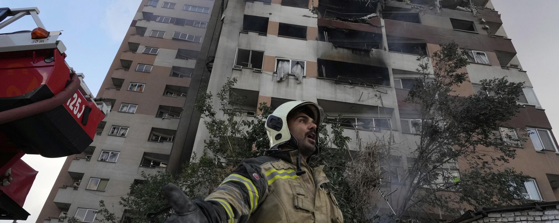 A firefighter calls out his colleagues at the scene of an explosion in a residence compound in northern Tehran, Iran, Friday, June 13, 2025.  - Sputnik International, 1920, 24.06.2025