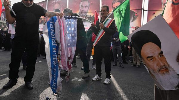 People burn the representations of the US and Israeli flags as a poster of the late Iranian revolutionary founder Ayatollah Khomeini is held at right during the funeral ceremony of Iranian armed forces generals, nuclear scientists and their family members killed in a 12-day war with Israel, in Tehran, Iran, Saturday, June 28, 2025.  - Sputnik International