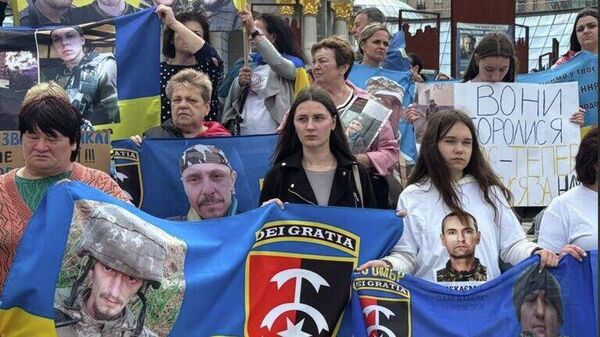 Protesters hold printed flag with soldiers faces and unit patches at Kiev protest demanding that the government provide closure on the fate of up to 2,000 troops listed as missing after hopeless 2023-2024 attack on Kherson. - Sputnik International