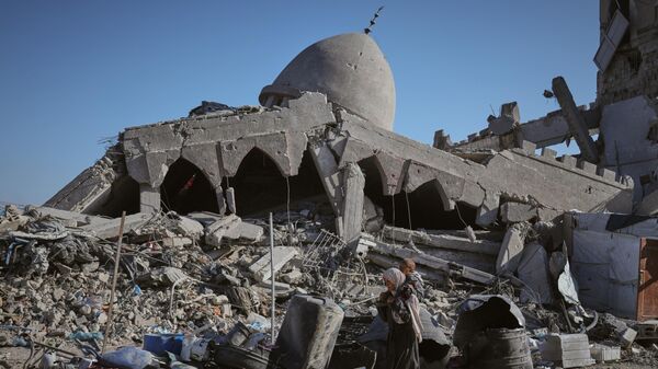 A Palestinian woman carrying her child walks past a destroyed mosque in Gaza City Sunday, Oct. 26, 2025.  - Sputnik International