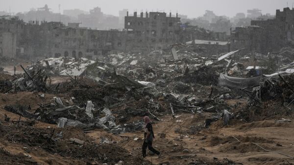 A Palestinian woman walks through a rainstorm past buildings destroyed in Israeli strikes in the Sheikh Radwan neighborhood of Gaza City, Friday, Nov. 14, 2025.  - Sputnik International