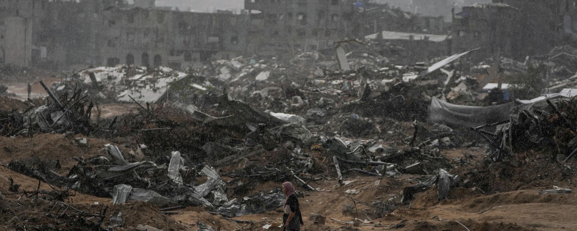 A Palestinian woman walks through a rainstorm past buildings destroyed in Israeli strikes in the Sheikh Radwan neighborhood of Gaza City, Friday, Nov. 14, 2025.  - Sputnik International, 1920, 15.11.2025