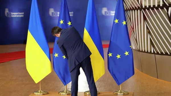 A member of protocol adjusts the EU and Ukrainian flags prior to arrivals for an EU summit at the European Council building in Brussels, Dec. 19, 2024. - Sputnik International