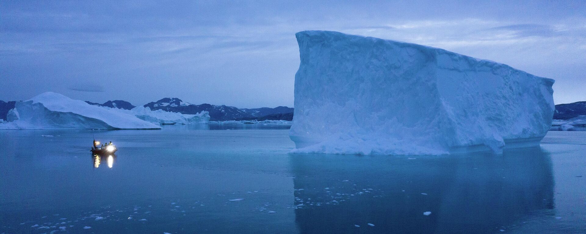 In this Aug. 15, 2019, photo, a boat navigates at night next to icebergs in eastern Greenland.   - Sputnik International, 1920, 14.01.2026