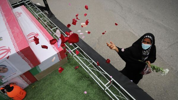 A woman throws rose petals on the coffins during funeral of mostly children killed in what Iranian officials said was an Israeli-U.S. strike Feb. 28 on a girls' elementary school in Minab, Iran, Tuesday, March 3, 2026. (Amirhossein Khorgooei/ISNA via AP) - Sputnik International