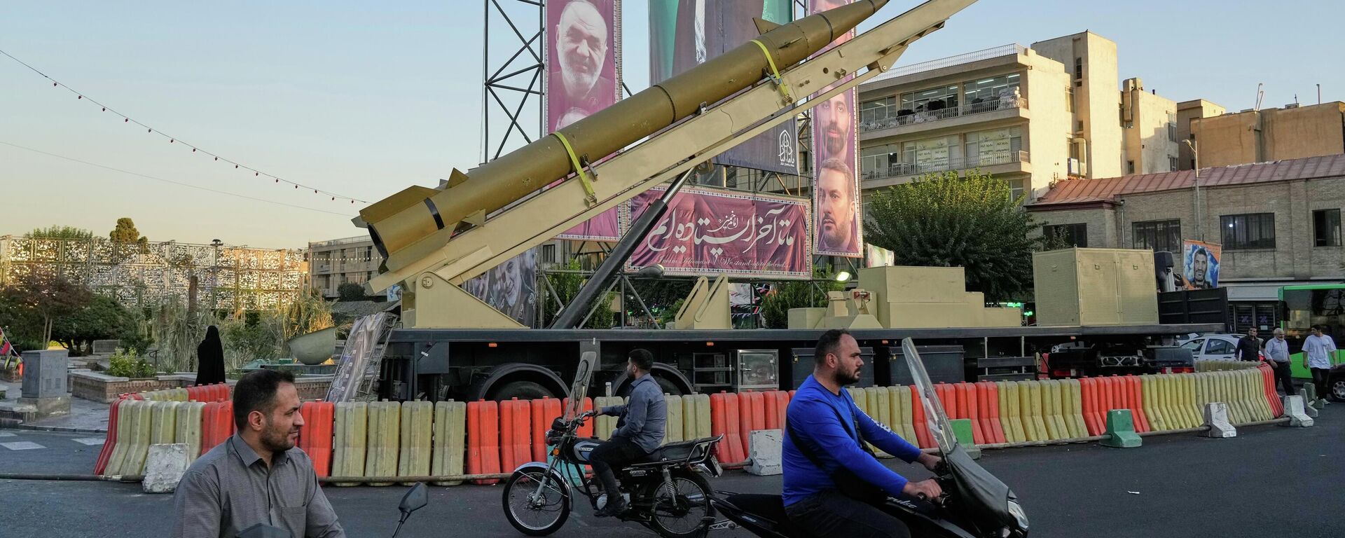 People drive past a domestically-built missile Khaibar-buster, and banners showing portraits of the now-late Iranian Supreme Leader Ayatollah Ali Khamenei, displayed in a military exhibition commemorating the anniversary of the start of the 1980-88 Iraq-Iran war, in Tehran, Sept. 25, 2025.  - Sputnik International, 1920, 04.03.2026