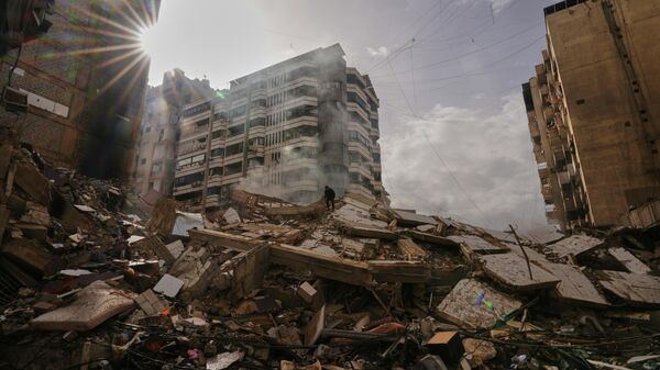A man stands atop the rubble as smoke rises from a building destroyed in an Israeli airstrike in Dahiyeh, Beirut's southern suburbs, Lebanon, Saturday, March 14, 2026. (AP Photo/Hassan Ammar) - Sputnik International