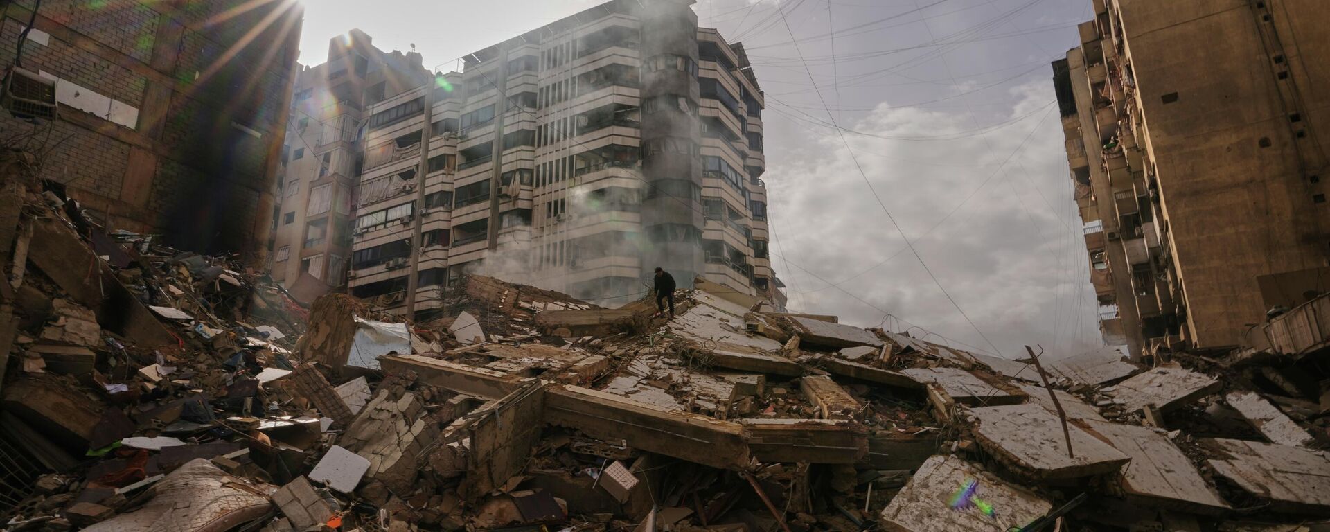 A man stands atop the rubble as smoke rises from a building destroyed in an Israeli airstrike in Dahiyeh, Beirut's southern suburbs, Lebanon, Saturday, March 14, 2026. (AP Photo/Hassan Ammar) - Sputnik International, 1920, 15.03.2026