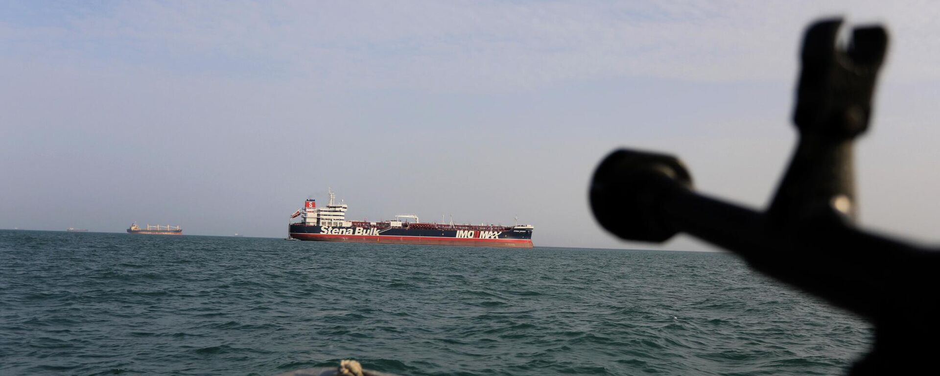 In this Sunday, July 21, 2019 photo, a speedboat of Iran's Revolutionary Guard trains a weapon toward the British-flagged oil tanker Stena Impero, which was seized in the Strait of Hormuz on Friday by the Guard, in the Iranian port of Bandar Abbas. Global stock markets were subdued Monday while the price of oil climbed as tensions in the Persian Gulf escalated after Iran's seizure of a British oil tanker on Friday.  - Sputnik International, 1920, 18.03.2026