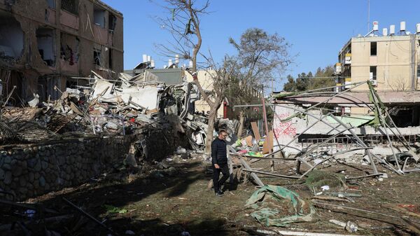 A man walks near debris from damage following a night of Iranian missile strikes which injured dozens of Israelis, amid the U.S.-Israel conflict with Iran, in Dimona, southern Israel, March 22, 2026. REUTERS/Ronen Zvulun - Sputnik International