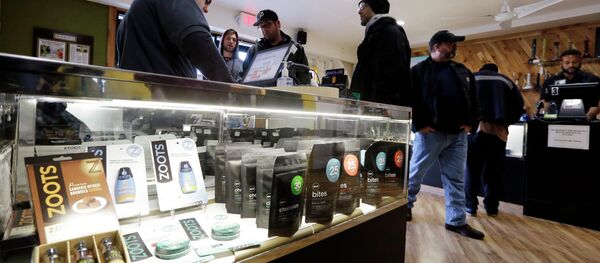 In this Tuesday, Dec. 30, 2014, photo, Cannabis City clerk John Golby, left, helps customers looking over a display case of marijuana products at the shop in Seattle. A year into the nation’s experiment with legal, taxed marijuana sales, Washington and Colorado find themselves with a cautionary tale for Oregon, Alaska or other states that might follow suit: They’re wrestling not with the federal interference many initially feared, but with competition from their own medical marijuana systems or even outright black market sales. - Sputnik International