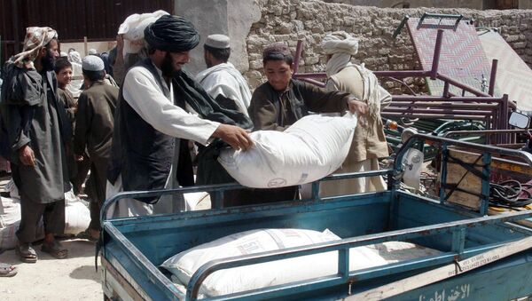Afghans put a sack of wheat on the carrier back of a motor bike during a food distribution to displaced families from Helmand province. - Sputnik International