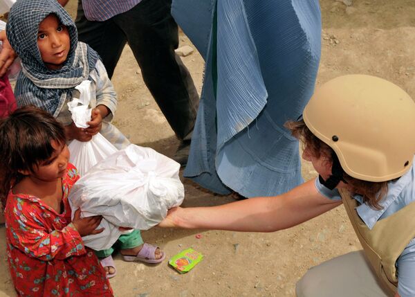 An Afghan girl accepts a bag of supplies from a volunteer duirng a humanitarian mission at an Afghan refugee camp - Sputnik International
