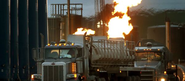 Drivers and their tanker trucks, capable of hauling water and fracking liquid line up near a natural gas burn off flame and storage tanks in Williston, N.D. Drivers and their tanker trucks, capable of hauling water and fracking liquid line up near a natural gas burn off flame and storage tanks in Williston, N.D. - Sputnik International
