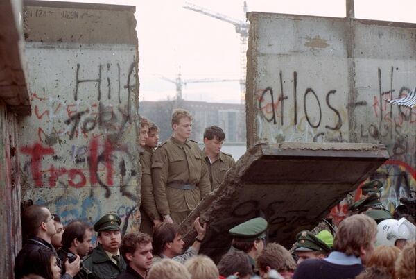 East German border guards look through a hole in the Berlin wall after demonstrators pulled down one segment of the wall at Brandenburg gate Saturday, November 11, 1989. East German border guards look through a hole in the Berlin wall after demonstrators pulled down one segment of the wall at Brandenburg gate Saturday, November 11, 1989. - Sputnik International