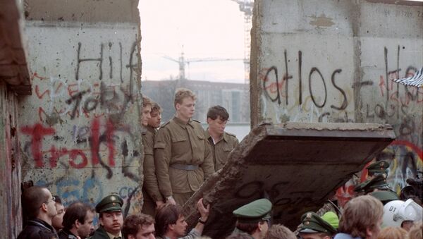 East German border guards look through a hole in the Berlin wall after demonstrators pulled down one segment of the wall at Brandenburg gate Saturday, November 11, 1989. - Sputnik International