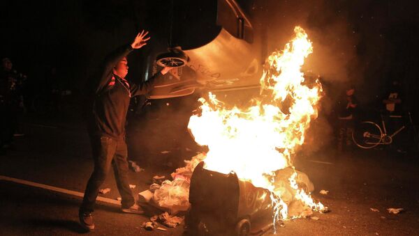 A protester throws a trash can on a fire during a demonstration in Oakland, California following the grand jury decision in the shooting of Michael Brown in Ferguson, Missouri - Sputnik International