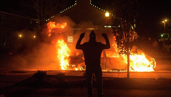 A man raises his arms in front of a burning police vehicle after a grand jury returned no indictment in the shooting of Michael Brown in Ferguson, Missouri - Sputnik International