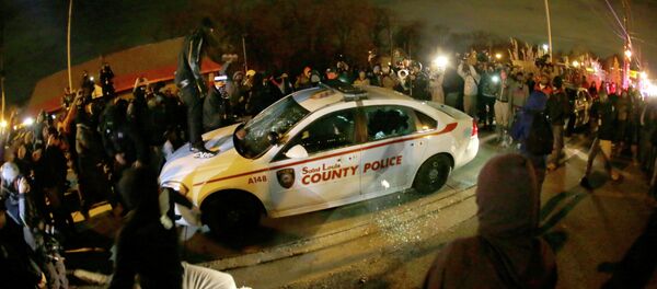 A protester squirts lighter fluid on a police car as the car windows are shuttered near the Ferguson Police Department after the announcement of the grand jury decision not to indict police officer Darren Wilson in the fatal shooting of Michael Brown, an unarmed black 18-year-old in Ferguson - Sputnik International