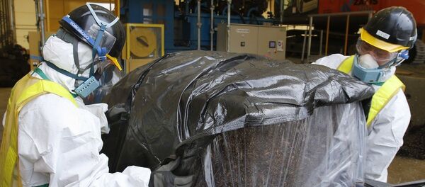Workers wearing protective gear wrap a compressed radioactive waste in a protective storage bag at a temporary waste storage site Workers wearing protective gear wrap a compressed radioactive waste in a protective storage bag at a temporary waste storage site - Sputnik International