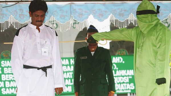 A masked religious official whips a convicted gambler with a rattan cane outside the main mosque in the town of Bireun, Aceh province, Indonesia. (File) - Sputnik International